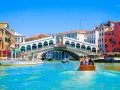Gondole e vaporetti solcano il Canal Grande, sotto il Ponte di Rialto affollato di gente. Un assaggio delle **esperienze Venezia**.