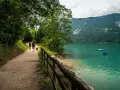 Coppia con cane passeggia lungo il sentiero del lago di Santa Croce, godendosi la natura e il panorama montano.