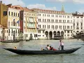 Gondola con turisti e gondoliere, sullo sfondo palazzi storici e altre barche tipiche veneziane.