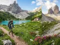 Escursionista solitario su sentiero fiorito, lago turchese e rifugio. Un'avventura di trekking Dolomiti 5 giorni indimenticabile.