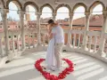 Un uomo abbraccia una donna su un balcone con vista su Venezia, circondati da petali di rosa a forma di cuore. Una perfetta proposta matrimonio Venezia.