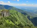 Panoramica mozzafiato dal Passo San Boldo, con verdi pendii montuosi che scendono verso una valle lontana sotto un cielo azzurro con nuvole bianche.