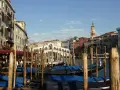 Gondole ormeggiate nel Canal Grande, con il Ponte di Rialto sullo sfondo. Un'immagine di Venezia romantica, con palazzi storici e il cielo azzurro.