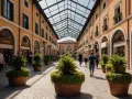 Passeggiata in una via dello shopping a Venezia, con portici, negozi e piante in vaso sotto un tetto di vetro.