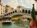 Traghetto della linea 2 di Venezia naviga sul Canal Grande sotto il Ponte di Rialto, con gondole e edifici storici sullo sfondo.