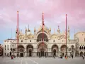 La maestosa basilica di San Marco a Venezia, con le sue cupole e mosaici dorati, si staglia sotto un cielo rosa al tramonto.
