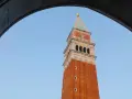 Vista dal campanile di San Marco: la torre in mattoni rossi si staglia contro il cielo azzurro, incorniciata da un arco di pietra.