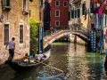 Gondola con turisti naviga in un canale, sotto un ponte, scoprendo la Venezia segreta tra palazzi antichi e fiori.