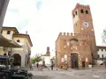 Piazza con torre medievale, portici e negozi. Ecco cosa vedere a Noale: la torre civica con orologio, il palazzo giallo e i tavolini all'aperto.