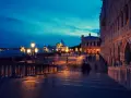 Venezia di notte, con le luci dei lampioni che illuminano la piazza e le sagome sfocate dei passanti.