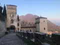 Antico borgo di Cison di Valmarino con torri e mura di pietra, sullo sfondo colline autunnali.