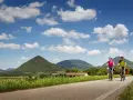 Coppia in bicicletta lungo la ciclabile dei Colli Euganei, tra verdi colline e cielo azzurro con nuvole bianche.