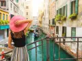 Donna con cappello rosa ammira un canale a Venezia, con gondole e palazzi storici. Un'esperienza da vivere a piedi, tra Santa Lucia e Piazza San Marco.