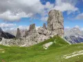 Sentiero che serpeggia tra verdi prati verso le maestose Cinque Torri Dolomiti, sotto un cielo azzurro con nuvole bianche.