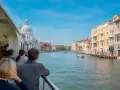 Gente sul vaporetto ammira il Canal Grande, con palazzi colorati e la Basilica di Santa Maria della Salute. Un viaggio tra Murano e Burano.