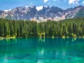 Lago alpino dalle acque turchesi, circondato da una fitta foresta di abeti, con le maestose cime delle Dolomiti innevate sullo sfondo. Un paesaggio da sogno, tra Venezia e le Dolomiti.