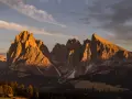 Le maestose **Dolomiti Rosse** illuminate dal sole al tramonto, con cime aguzze e pendii boscosi.