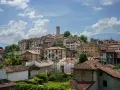 Panoramica di Feltre e dintorni, con case dai tetti rossi che si arrampicano sulla collina sotto un cielo azzurro e nuvoloso.