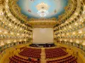 Interno sfarzoso del Teatro La Fenice di Venezia, con palchi dorati, soffitto affrescato e un grande schermo bianco.
