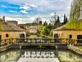 Ponte in legno su un canale con mulini ad acqua, case storiche e vegetazione rigogliosa, un'atmosfera serena che ricorda Portogruaro Caorle.