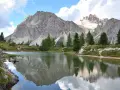 Riflessi perfetti delle montagne nel **lago di Limedes**, con sentiero e pini che incorniciano il paesaggio.