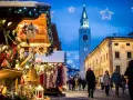 Mercatino di Natale a Cortina d'Ampezzo, con bancarelle addobbate, luci scintillanti e la torre del campanile che domina il cielo serale.