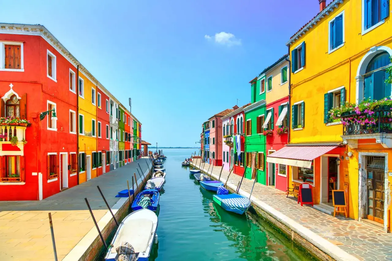 Coloratissima isola a Venezia, con case vivaci affacciate su un canale pieno di barche.