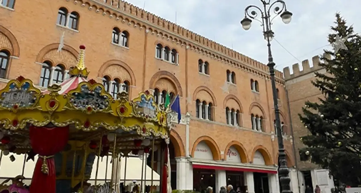 Carosello colorato e albero di Natale in piazza, scorci di cosa vedere a Treviso con palazzi storici e gente che passeggia.
