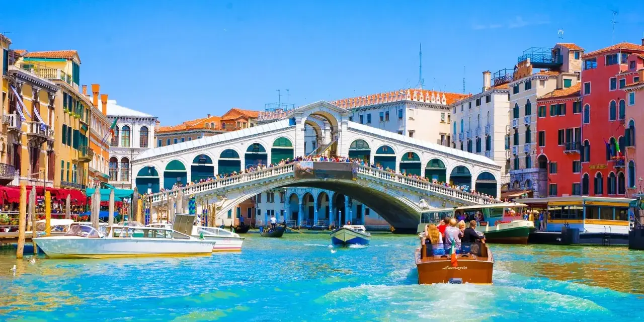 Gondole e vaporetti solcano il Canal Grande, sotto il Ponte di Rialto affollato di gente. Un assaggio delle **esperienze Venezia**.