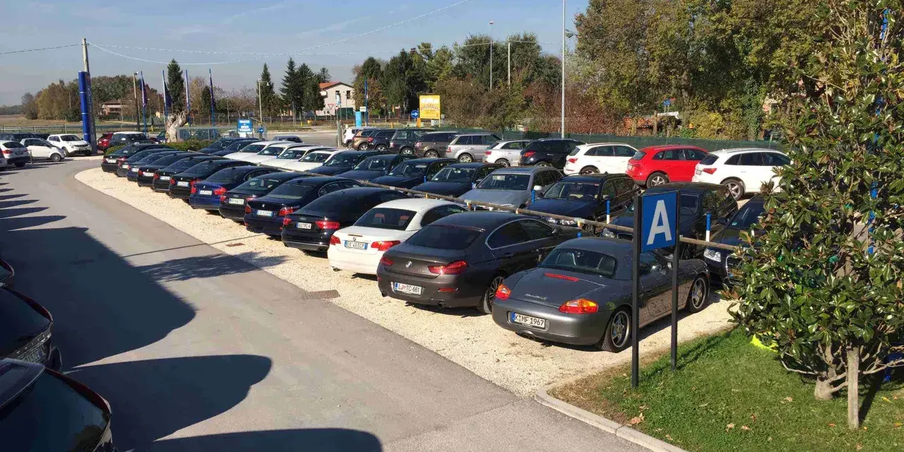 Parcheggio con auto moderne, forse vicino a Venezia Mestre o Santa Lucia. Un cartello blu con la "A" indica un'area di sosta.