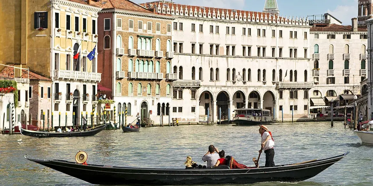 Gondola con turisti e gondoliere, sullo sfondo palazzi storici e altre barche tipiche veneziane.