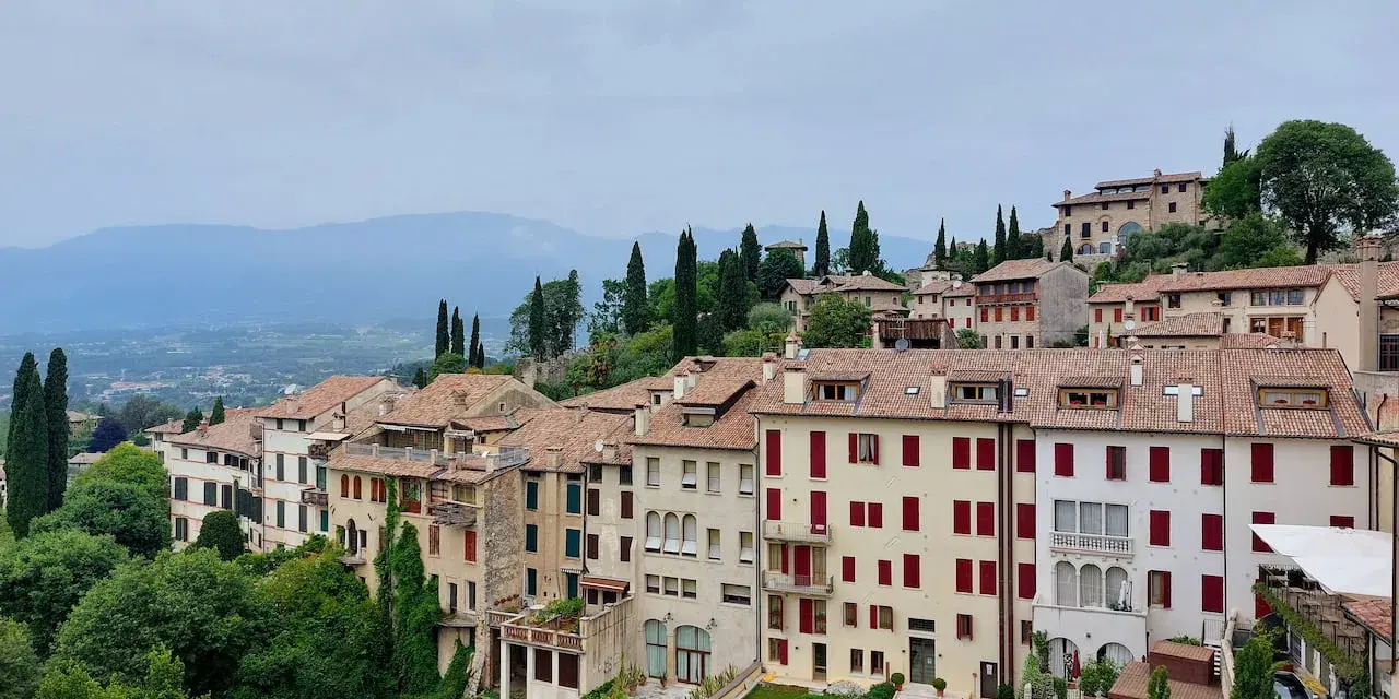 Asolo, cosa vedere: un borgo collinare con case in pietra, tetti rossi e giardini lussureggianti, incastonato tra le montagne.