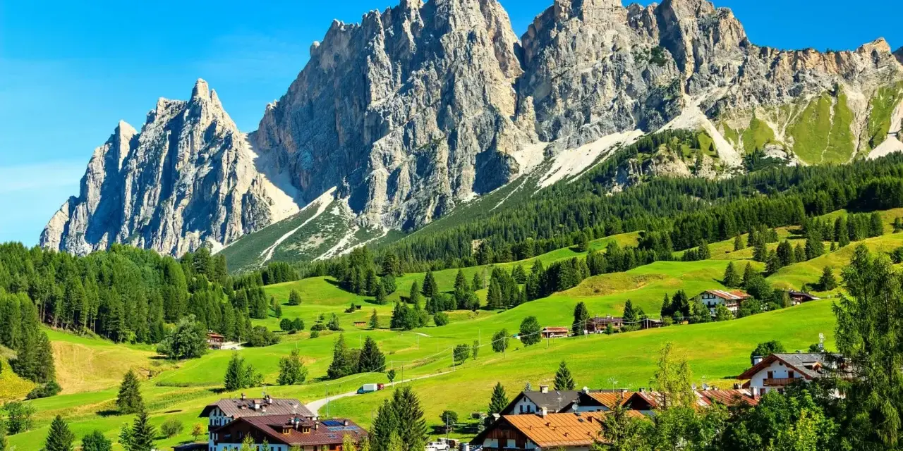 Un viaggio da Venezia a Cortina: verdi pascoli, boschi rigogliosi e imponenti vette dolomitiche incorniciano un villaggio alpino.