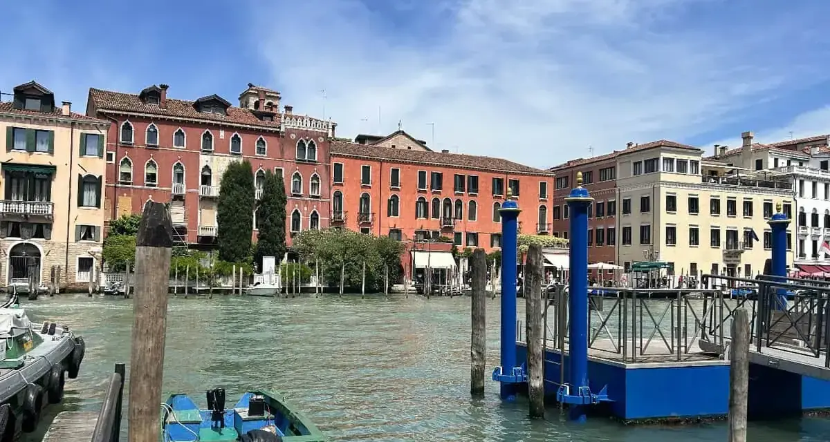 Canale di Venezia con edifici colorati e pontili blu. Per sapere how to get from Venice train station to San Marco, prendi un vaporetto.