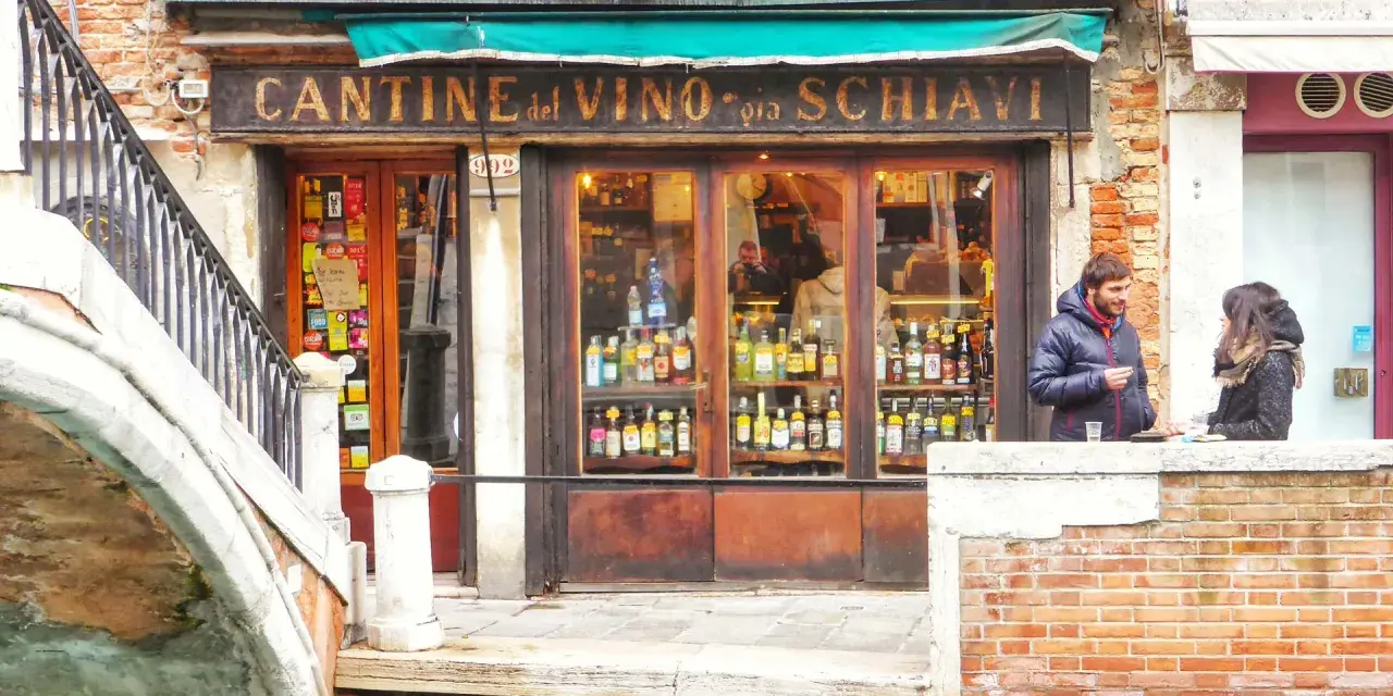 Coppia davanti a una delle tipiche osterie a Venezia, con bottiglie di vino in esposizione.