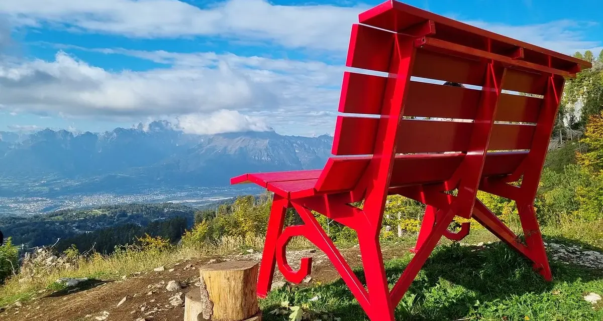 La panchina gigante sul Nevegal, rossa e imponente, domina un panorama mozzafiato di montagne e vallate sotto un cielo azzurro.