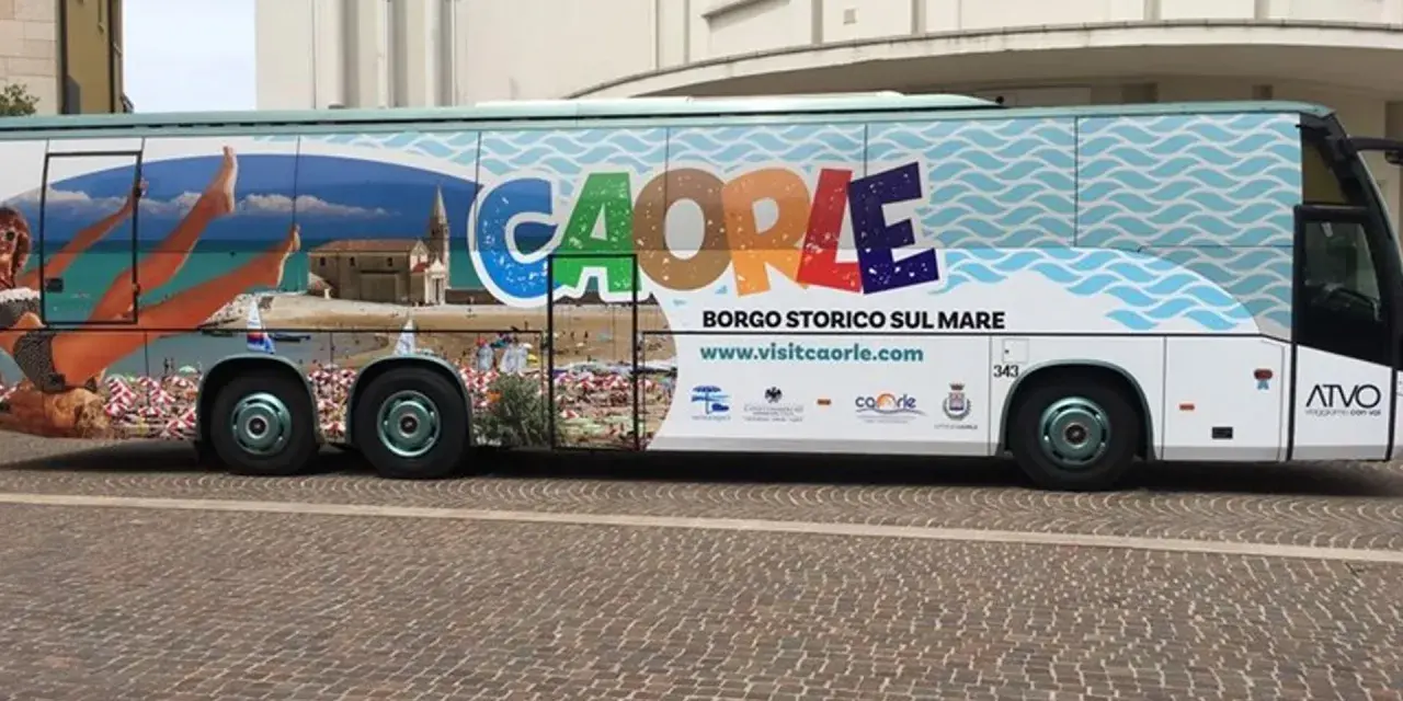 Bus turistico con grafica promozionale di Caorle, borgo storico sul mare. Immagini di spiaggia, mare e una donna in bikini.