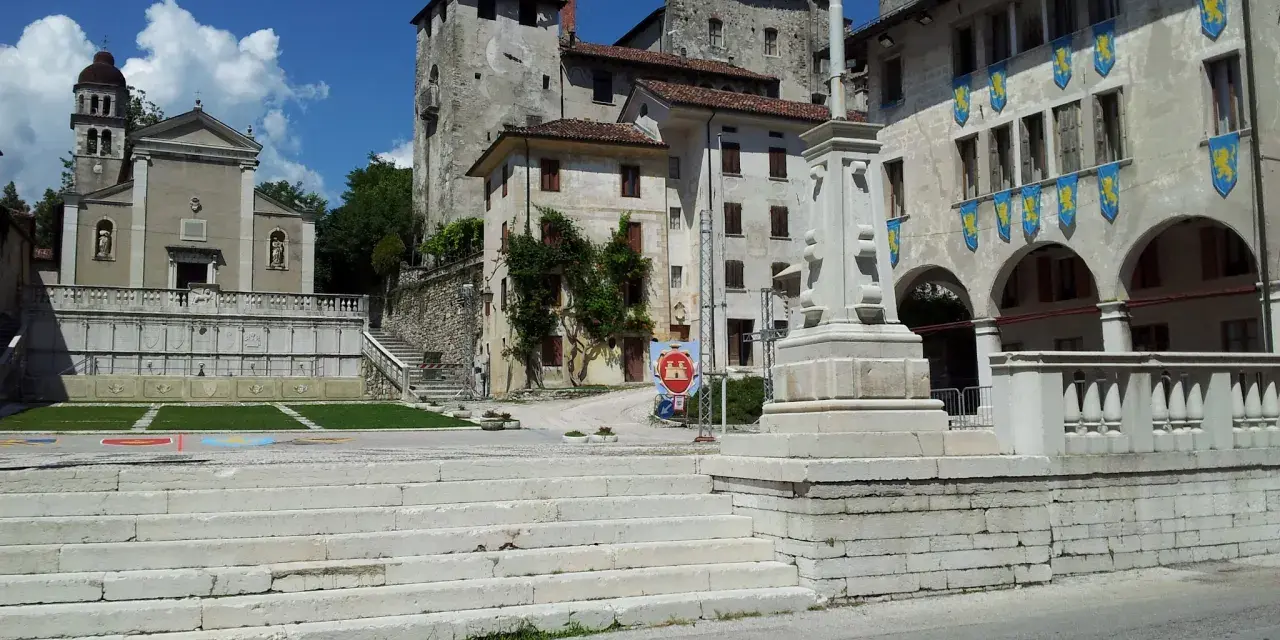 Piazza con scalinata, chiesa e castello: ecco cosa vedere a Feltre. Stendardi gialli decorano gli edifici storici.