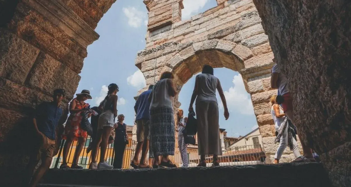 Turisti esplorano l'Arena di Verona, un'antica struttura che ricorda il Colosseo, sotto un cielo azzurro.
