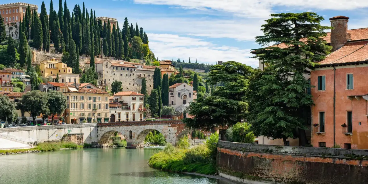 Un fiume attraversa Verona, con ponti storici e case colorate che salgono sulla collina. Un luogo incantevole da scoprire, tra le cose da vedere a Verona.