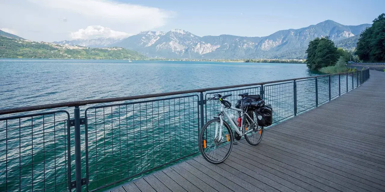 Bicicletta da turismo pronta per esplorare le ciclabili Dolomiti, con un lago azzurro e montagne maestose sullo sfondo.