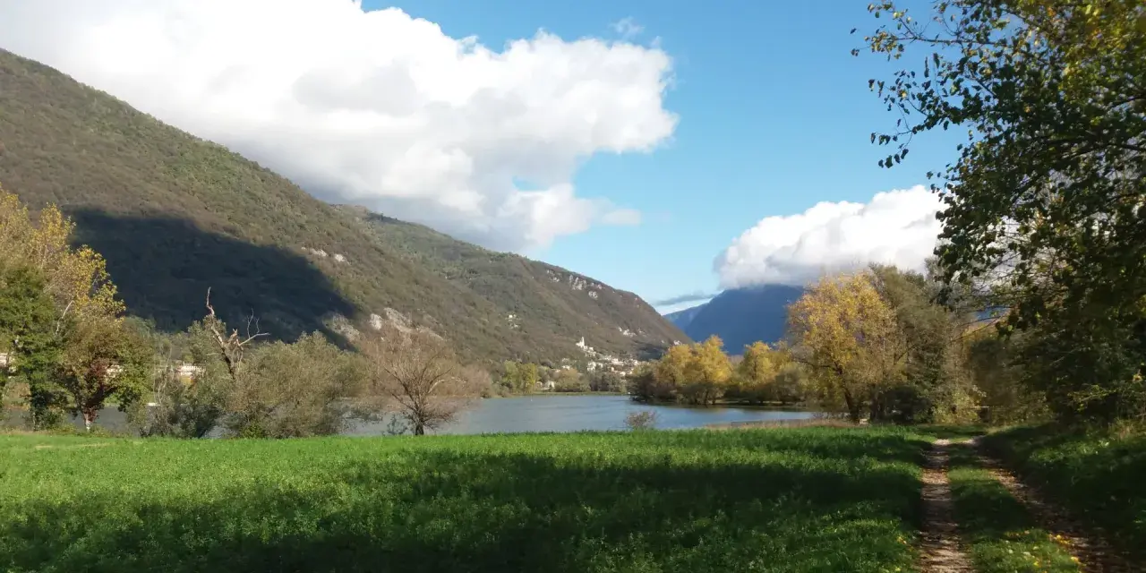 Sentiero per passeggiate in montagna Veneto, con lago, colline verdi e cielo azzurro con nuvole bianche.
