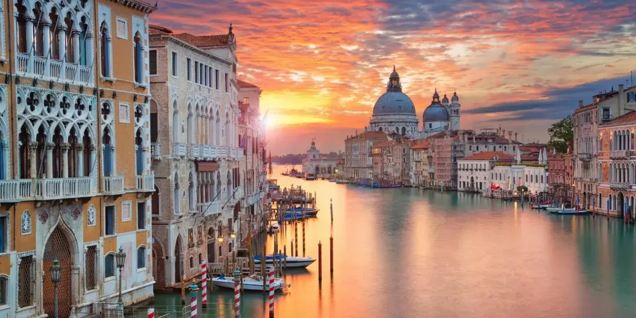 Tramonto sul Canal Grande, un quadro perfetto di posti romantici a Venezia. Palazzi storici e la Basilica di Santa Maria della Salute riflettono i colori del cielo.