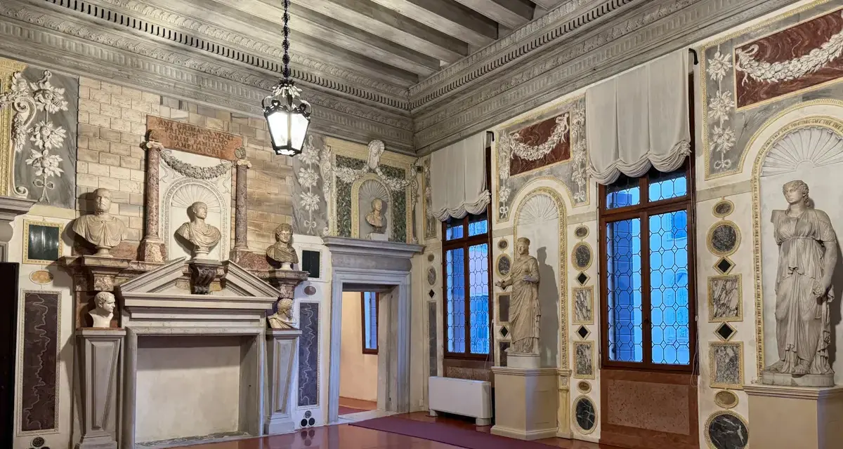 Interni del Palazzo Grimani: busti, statue, camino e finestre decorate in un salone sontuoso.