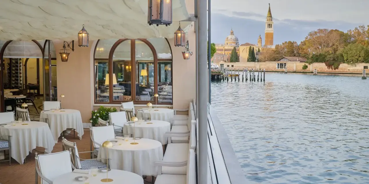 Terrazza elegante di uno dei ristoranti famosi a Venezia, con tavoli apparecchiati e vista sul canale e sulla città.