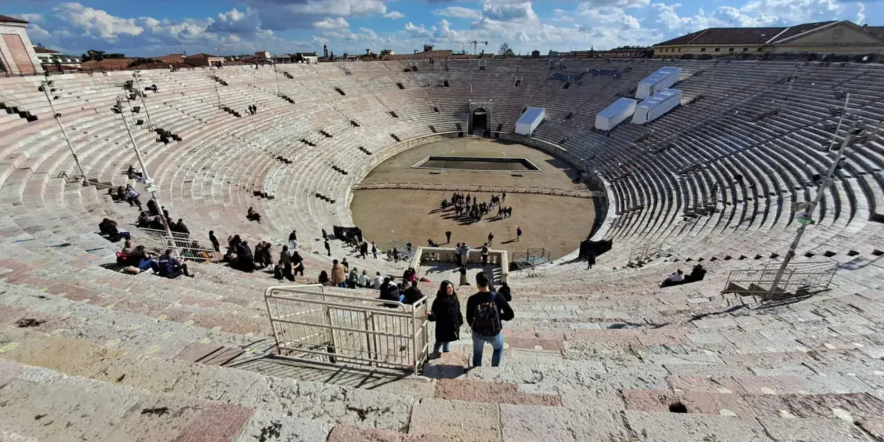 L'**arena di Verona colosseo** romano, con le sue gradinate affollate di turisti, sotto un cielo azzurro e nuvoloso.