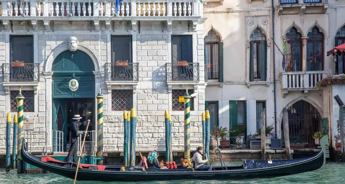 Gondola con gondoliere e passeggeri naviga lungo un canale a Venezia. Esplorare Venezia a piedi è un'esperienza, ma una gondola offre una prospettiva unica.