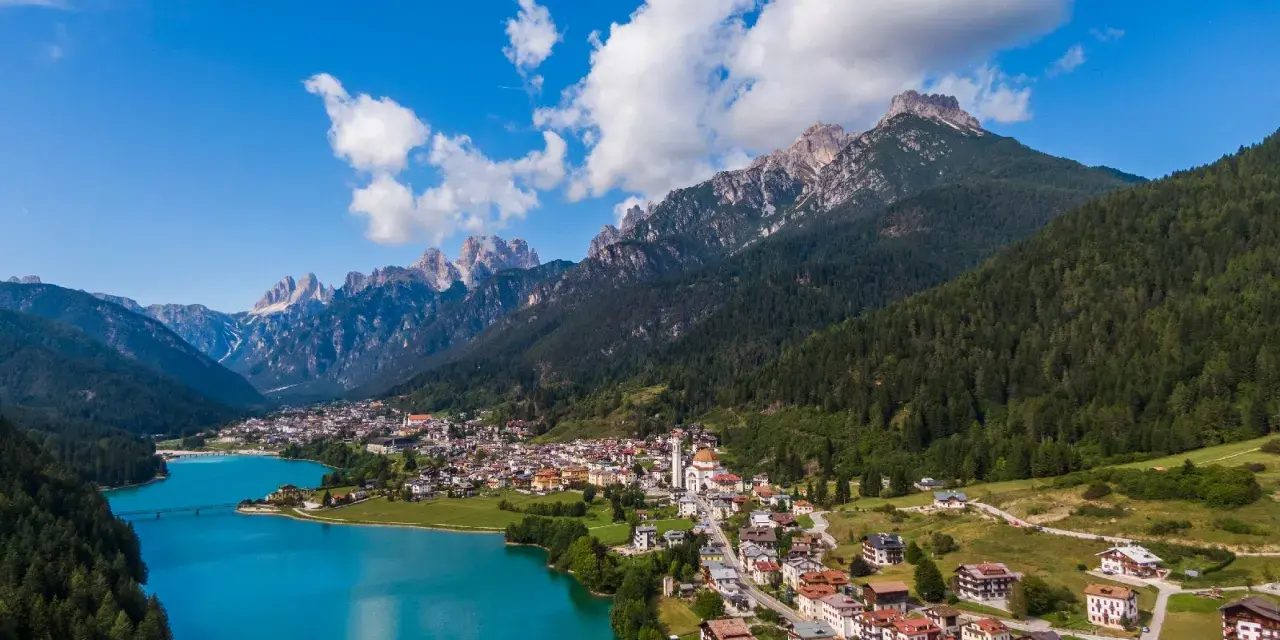 Vista aerea del **lago Auronzo di Cadore** con le montagne sullo sfondo e il paese che si affaccia sull'acqua turchese.