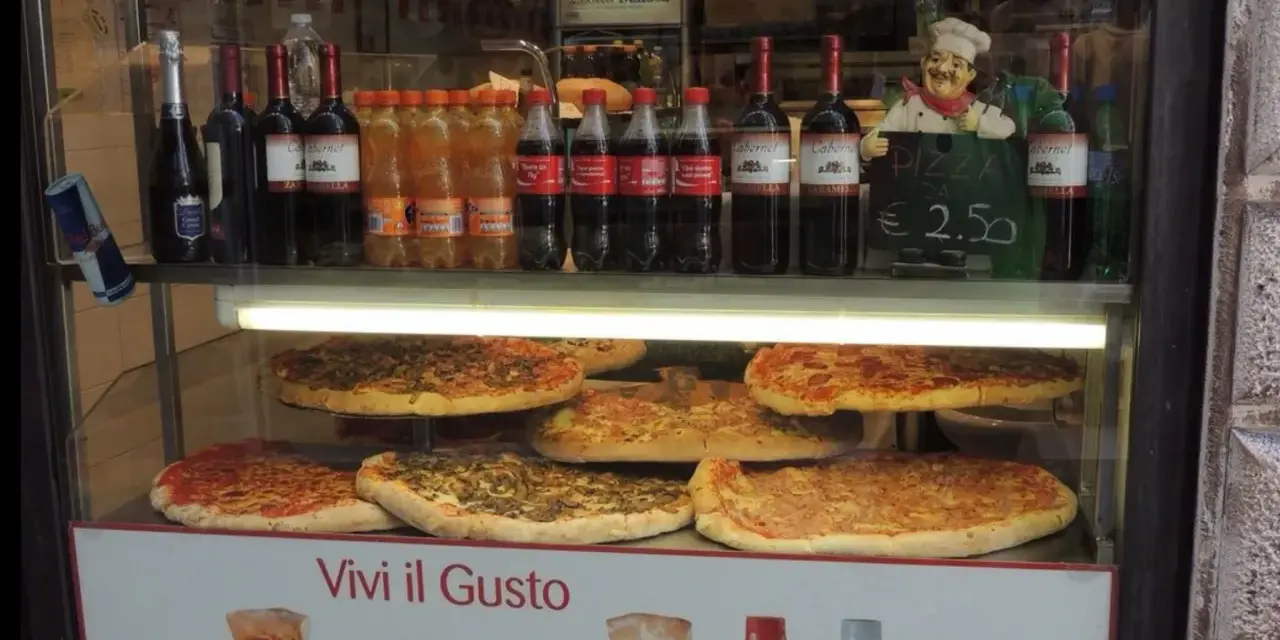 Vetrine con pizze, bottiglie di vino e bibite, un cartello "PIZZA DA € 2.50" e un cuoco decorativo. Sembra un ottimo posto per trovare le migliori pizzerie a Venezia.