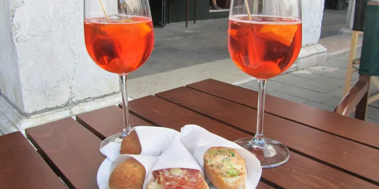 Due calici di Spritz e cicchetti, un classico per gli aperitivi a Venezia, su un tavolino di legno.